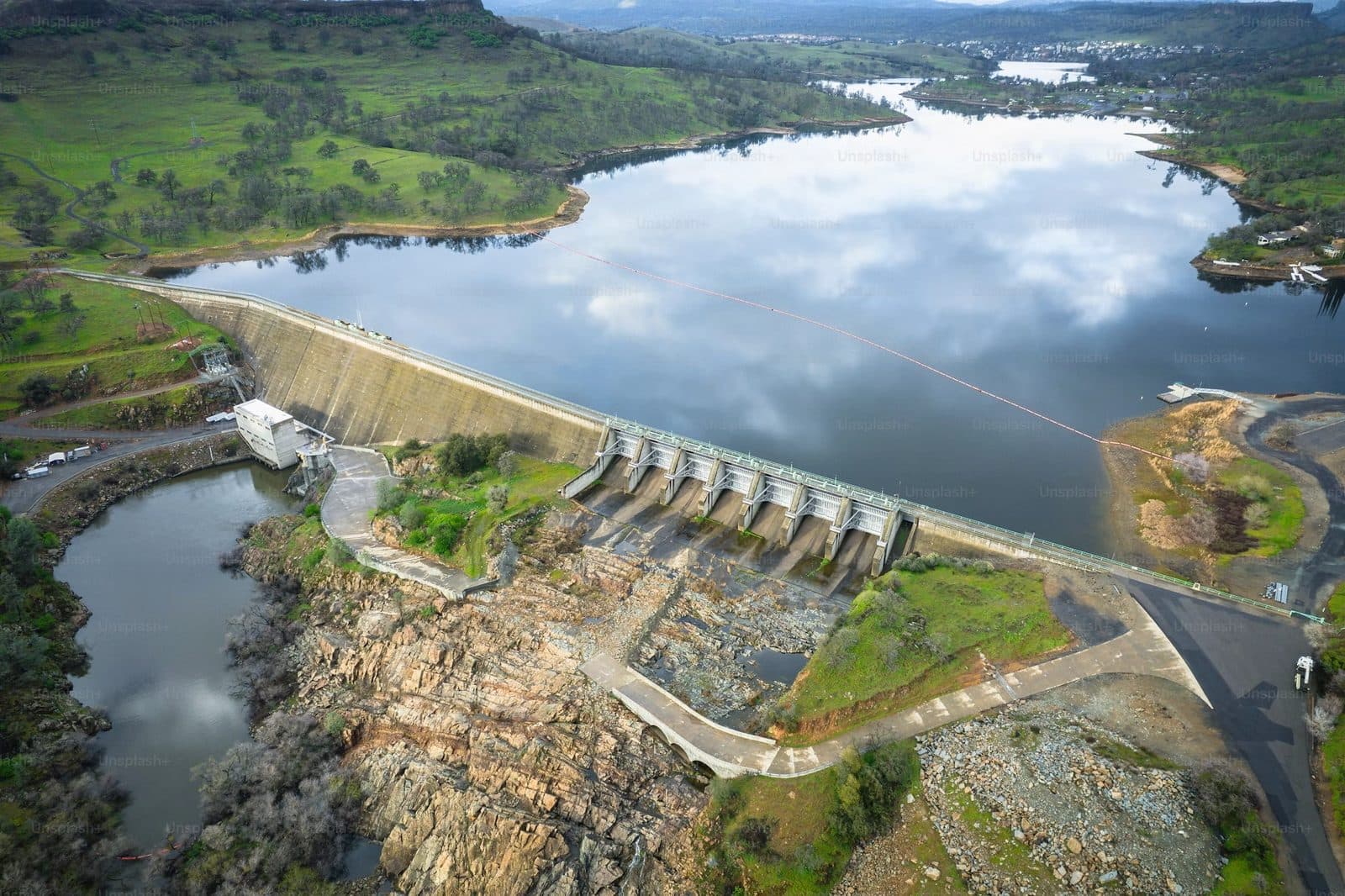 Aerial view of a hydroelectric dam with a reservoir reflecting clouds